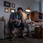 A father and son play video games on their living room couch.