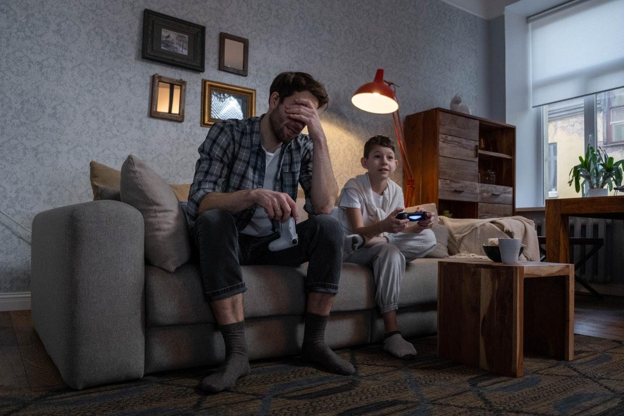 A father and son play video games on their living room couch.